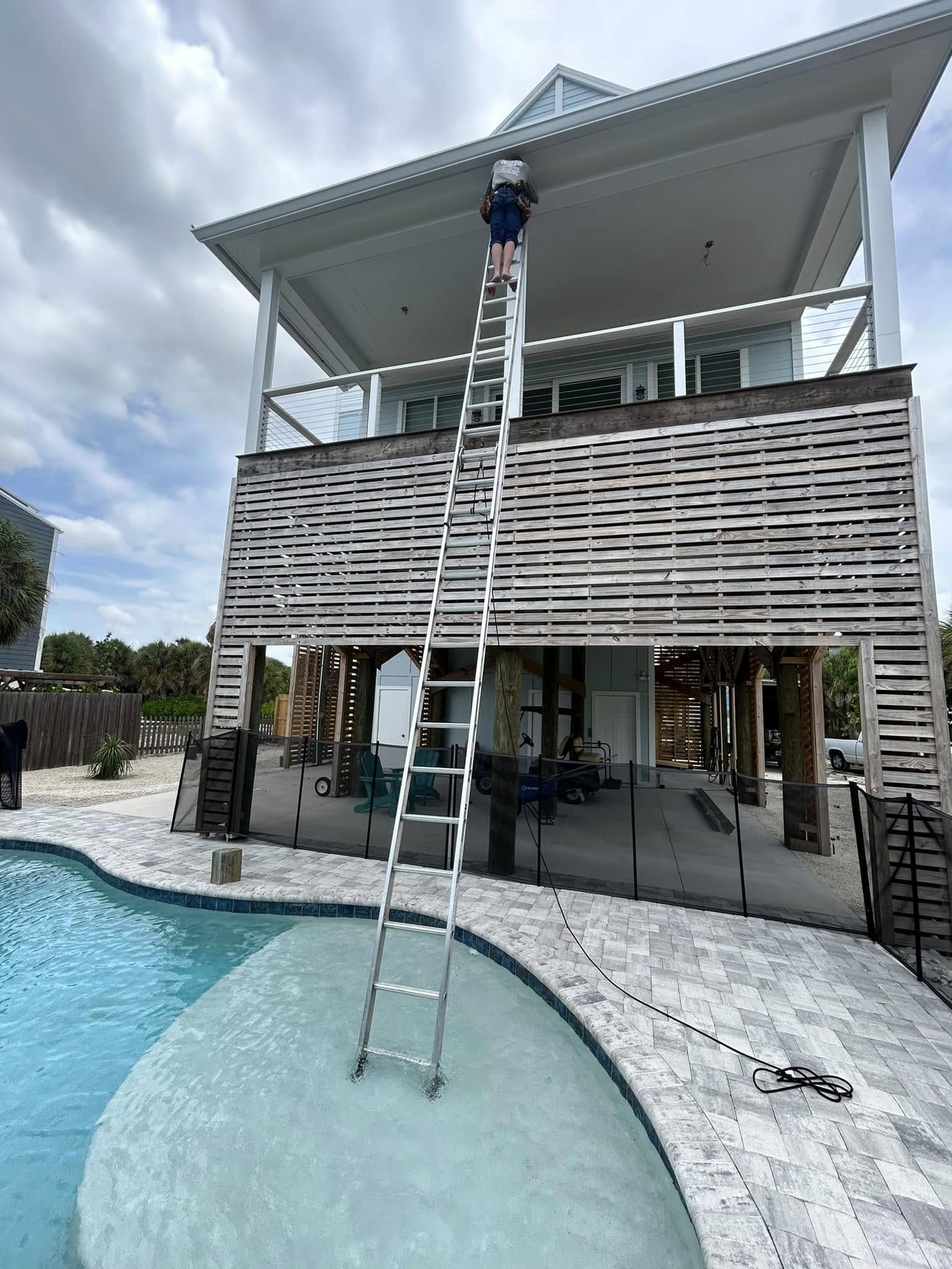 Installer up on a ladder installing seamless gutters on the second story of a florida coastal house
